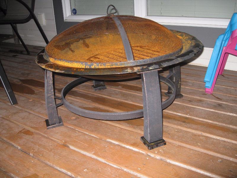 Rusted firepit with cooking grill and 2 boxes of wood